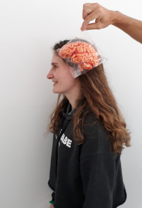 Female scientist standing. Chocolate brain held in front of head.