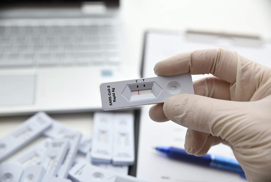 Scientist holding a covid-19 rapid antigen test, with several more rapid antigen tests in the background.